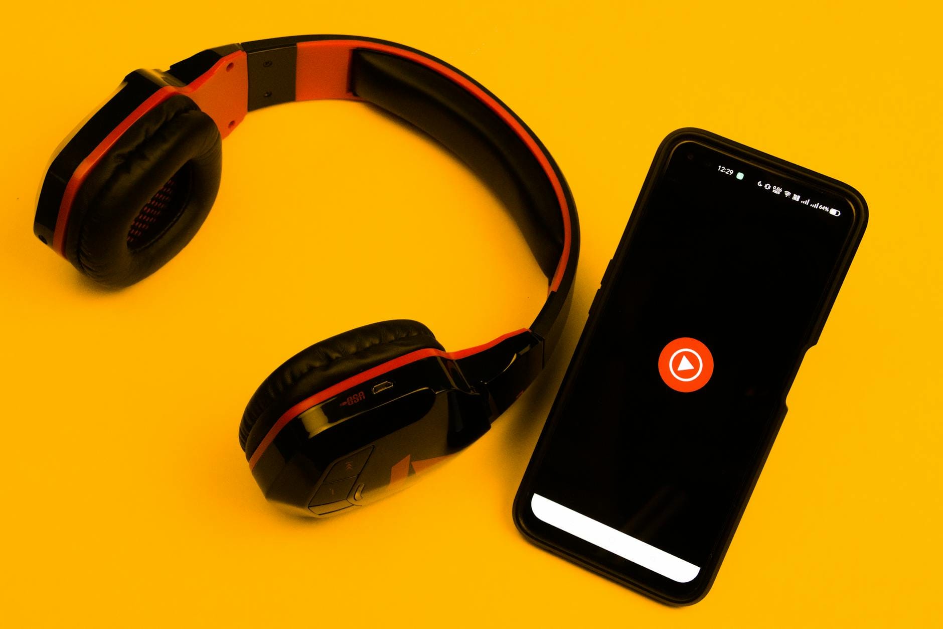 Bezprzewodowe słuchawki i smartfon z ikoną play na żółtym tle