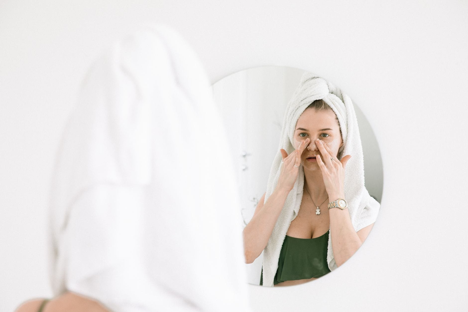 Kobieta w ręczniku nakłada naturalne kosmetyki przed lustrem w łazience