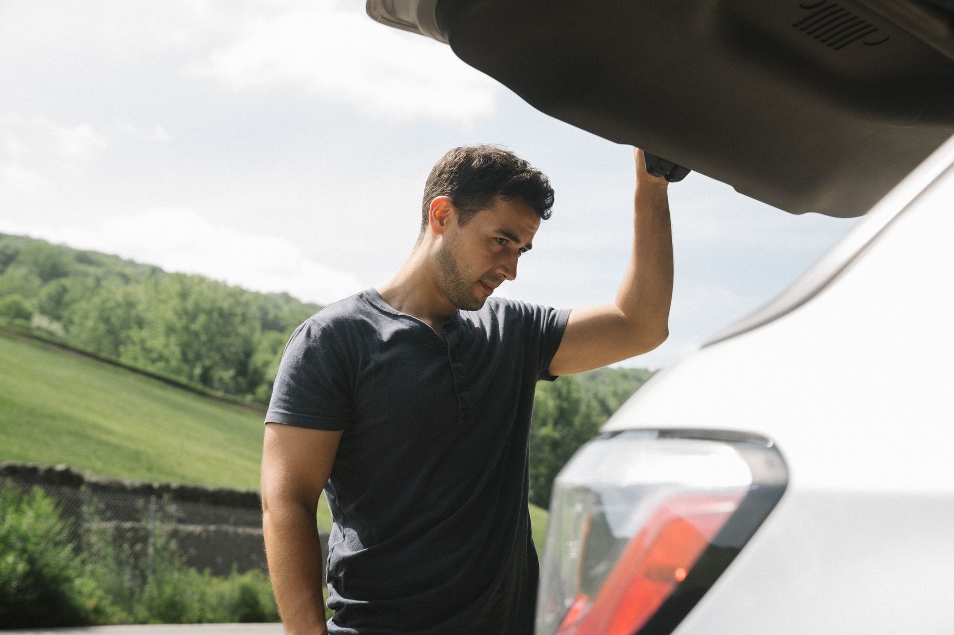 Jak przygotować auto na długą trasę: przegląd przed wyjazdem, niezbędne wyposażenie i praktyczne porady kierowcy Mężczyzna sprawdzający bagażnik auta przed wyjazdem w słoneczny dzień