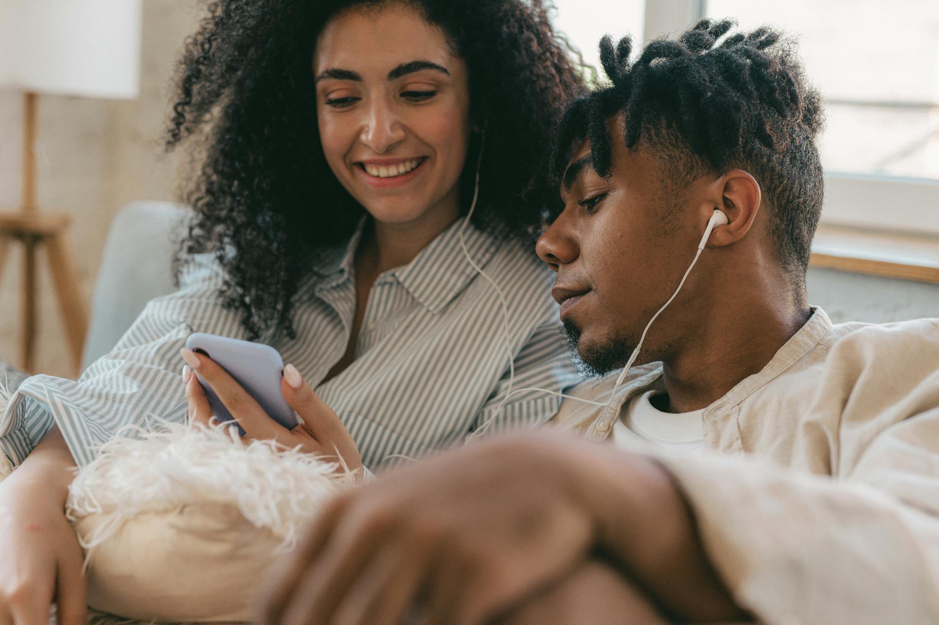 Uśmiechnięta para w domu słucha audiobooka na smartfonie