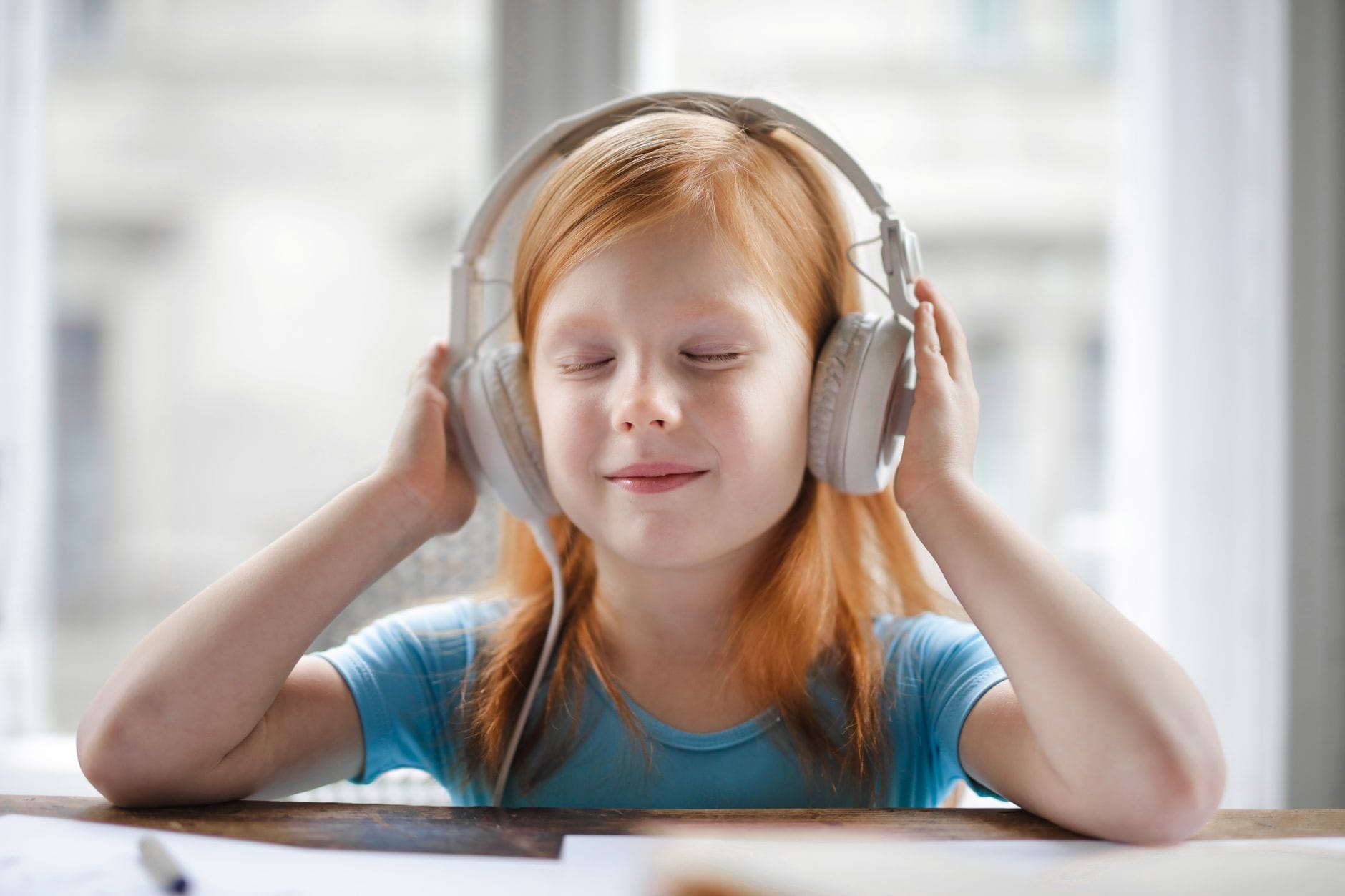 Dziewczynka w słuchawkach słucha audiobooka i uśmiecha się w domu