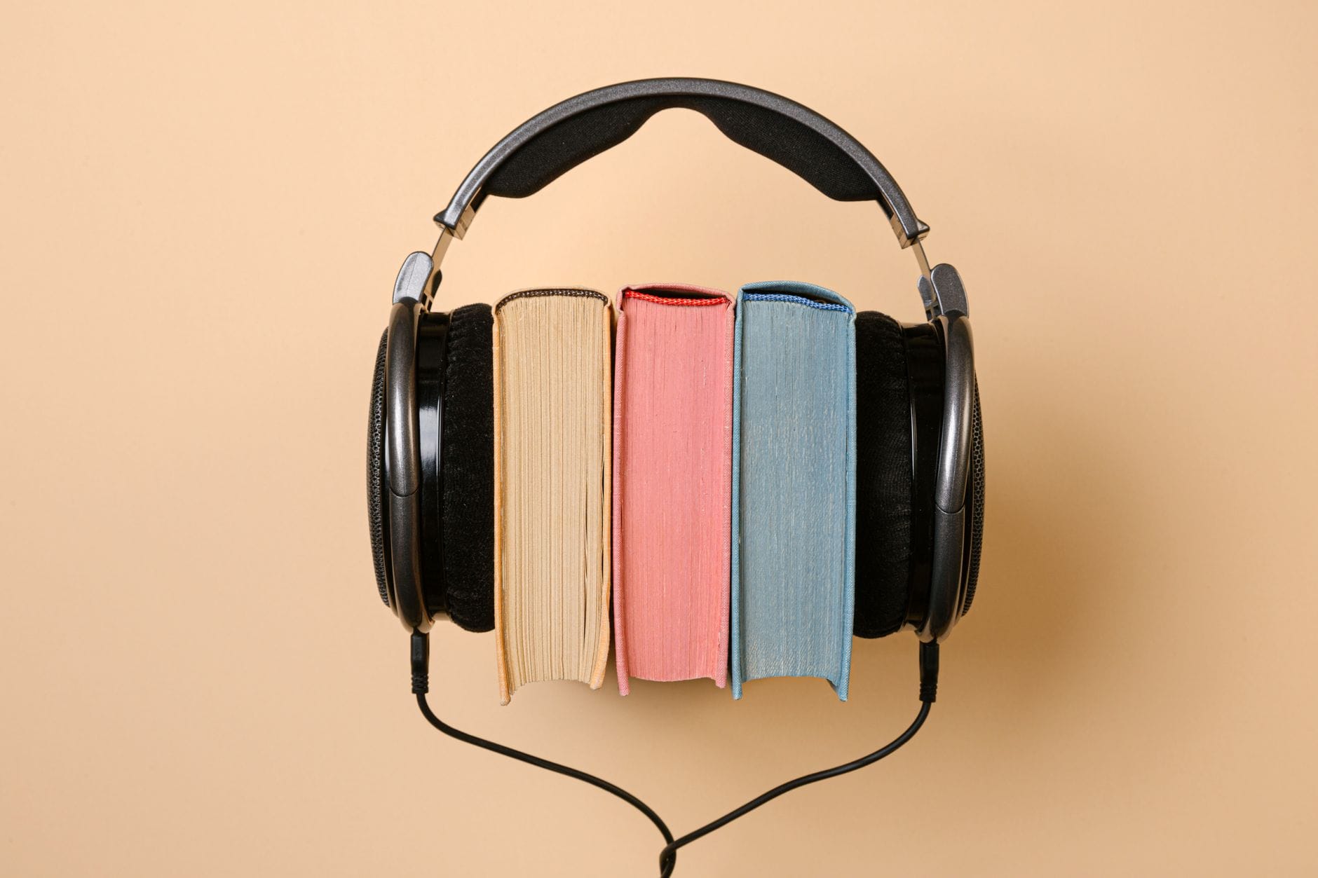 Słuchawki na stosie książek na beżowym tle, symbol nauki z audiobooków