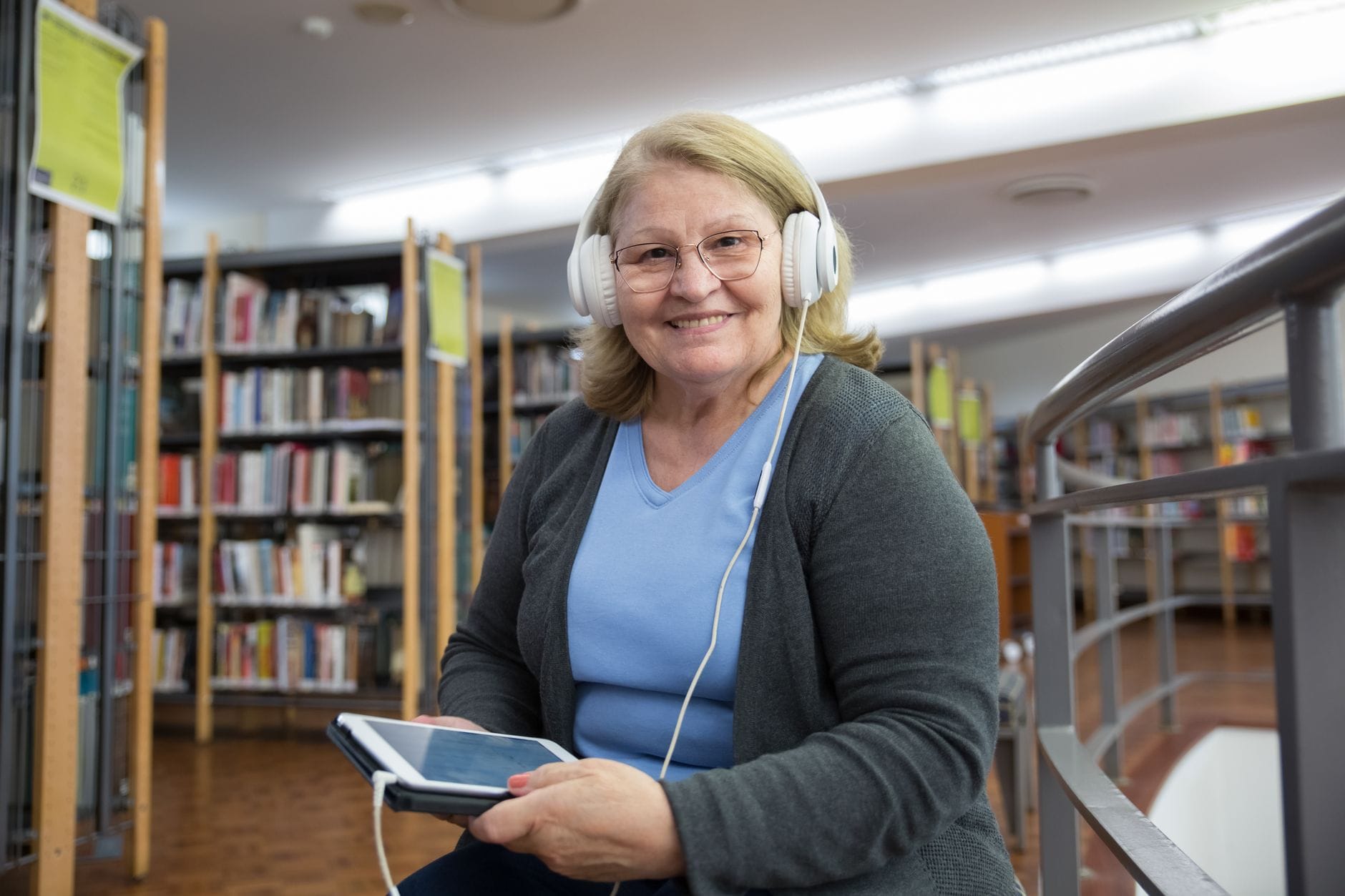 Starsza kobieta słuchająca audiobooka na tablecie w bibliotece Starsza kobieta słuchająca audiobooka na tablecie w bibliotece