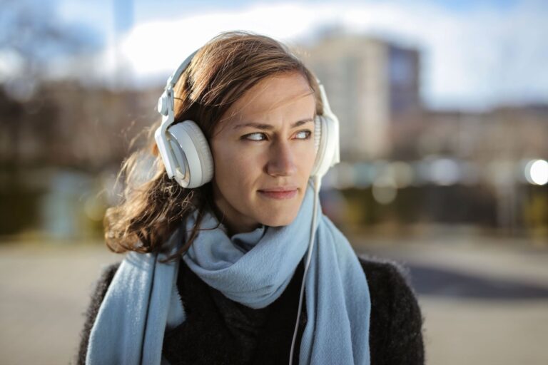 Młoda kobieta w słuchawkach i szaliku słucha audiobooka zimą na zewnątrz